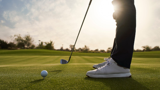 golf ball and club on green with the feet of a golfer