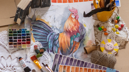 Painting supplies and a painting of a cockerel