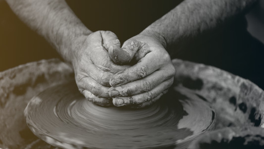 potter's hand around a lump of clay on a potter's wheel