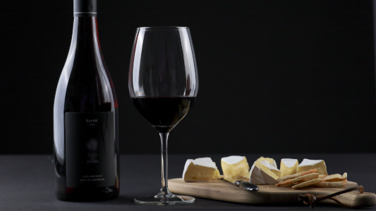 Bottle or red wine with a glass and a plate of cheese