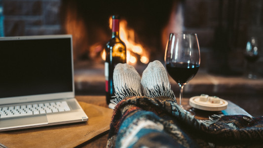  A laptop on a table in front of a fireplace with a pair of feet in the table