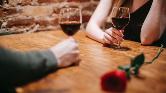 two people at a table, each holding a glass of red wine 
